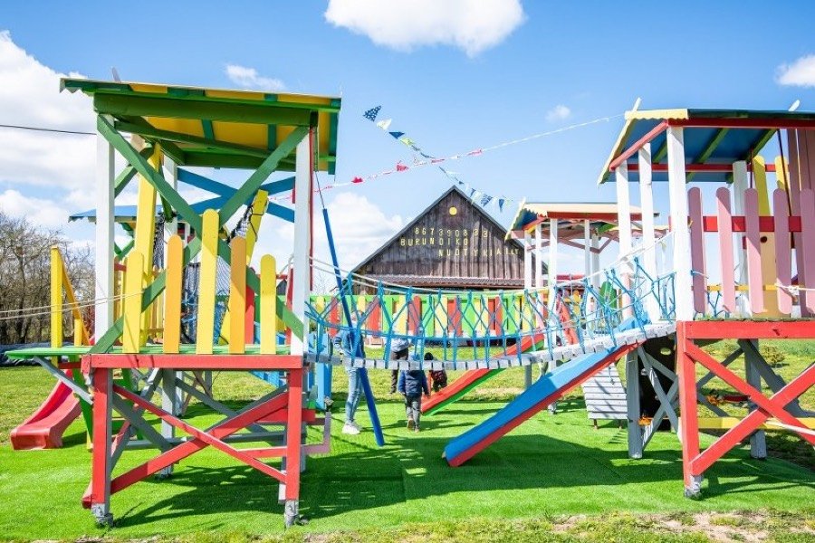 Spalvotas medinis žaidimų parkas su čiuožyklomis ir tiltais po žydru dangumi